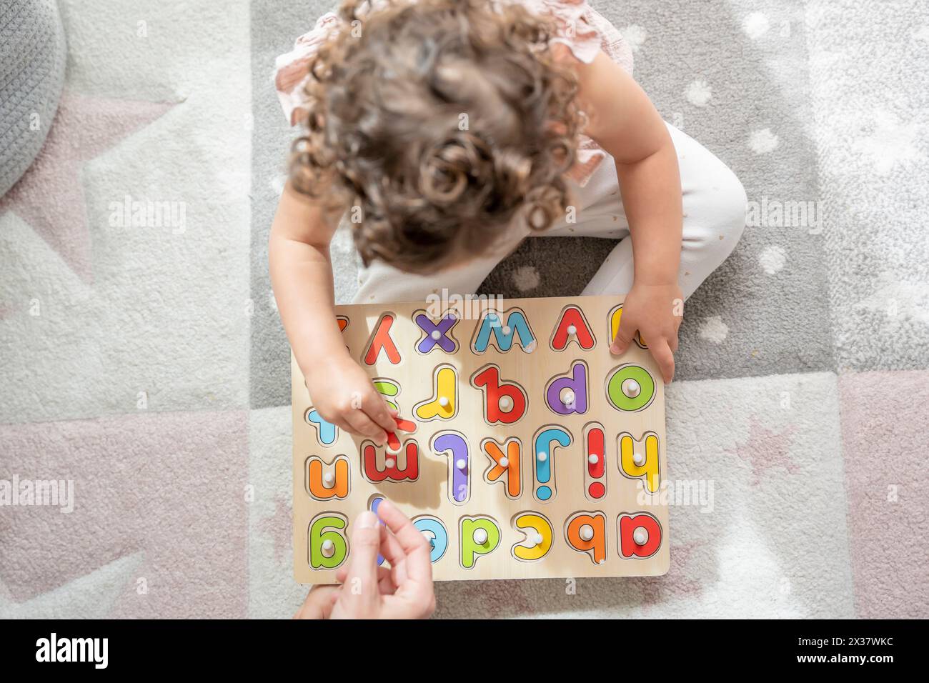 vue aérienne d'une fille interagissant avec sa mère assise sur le sol de sa chambre avec un puzzle de lettres en bois. Montessori méthodologie et éducation Banque D'Images