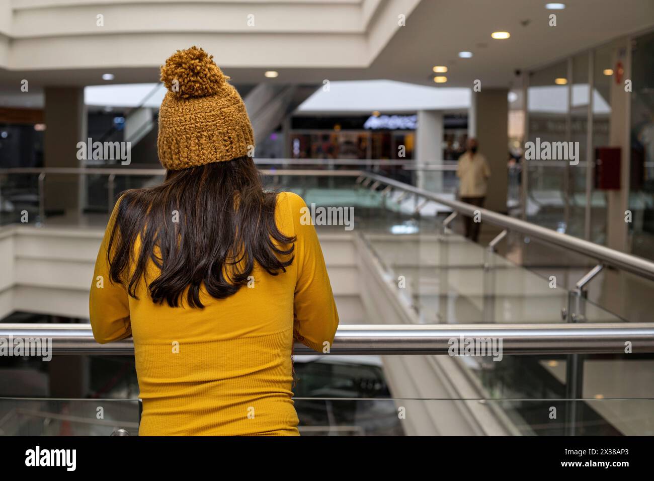 Jeune femme latino-américaine (23 ans) se tient dos à la rampe du centre commercial, portant une casquette jaune et de la flanelle. Banque D'Images