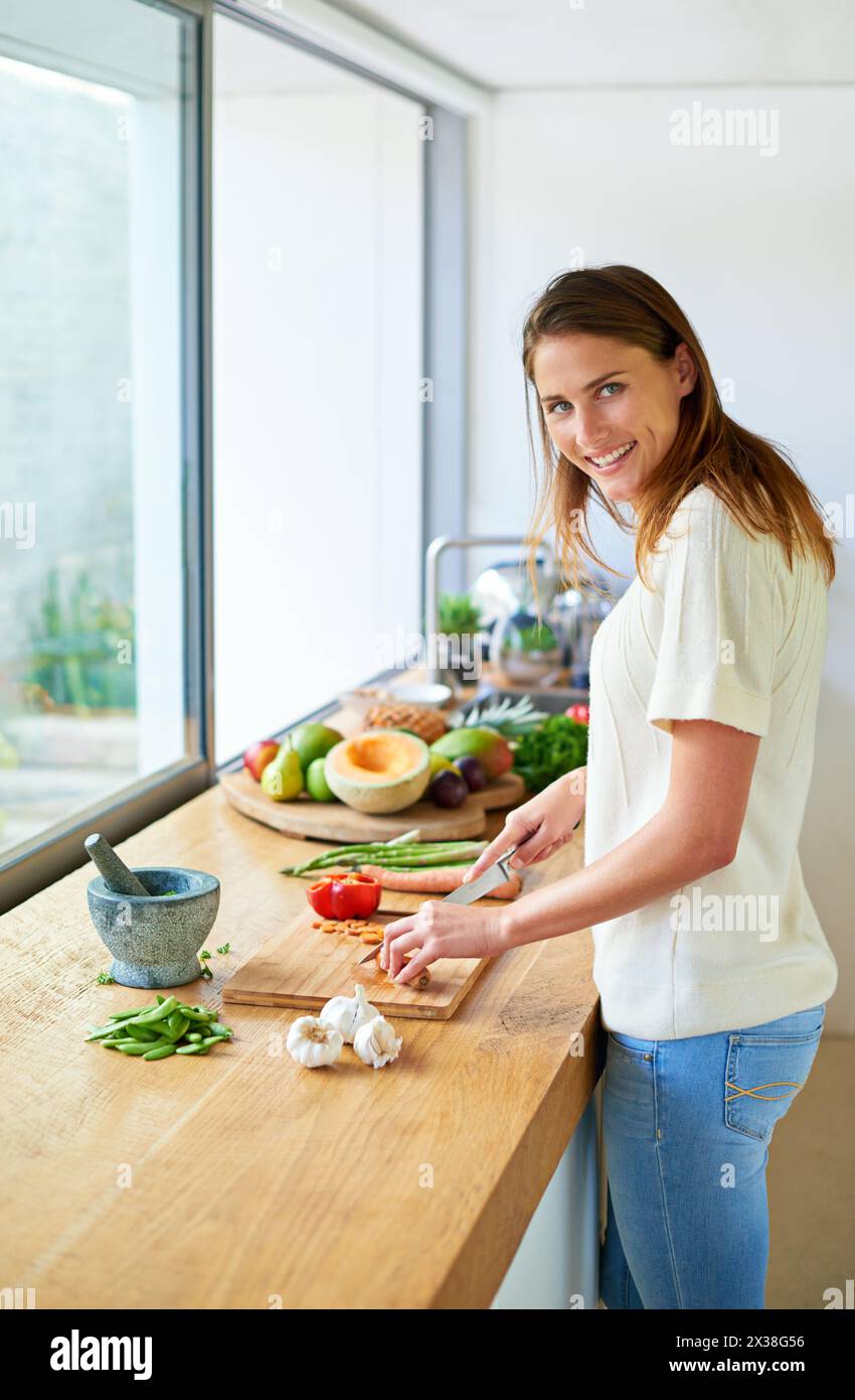 Portrait, maison et femme avec des légumes, coupe et sourire avec végétalien, repas sain et nutrition. Visage, végétarien et personne dans la cuisine, la nourriture et Banque D'Images