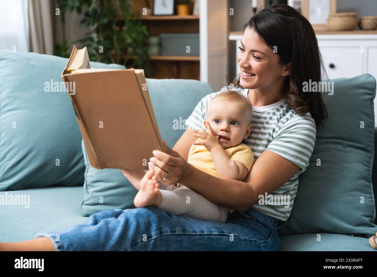 Jeune mère heureuse lisant un livre de conte de fées à son bébé. Maman et enfant assis sur le canapé à la maison profitant de l'imagination. Vie parent et enfant Banque D'Images