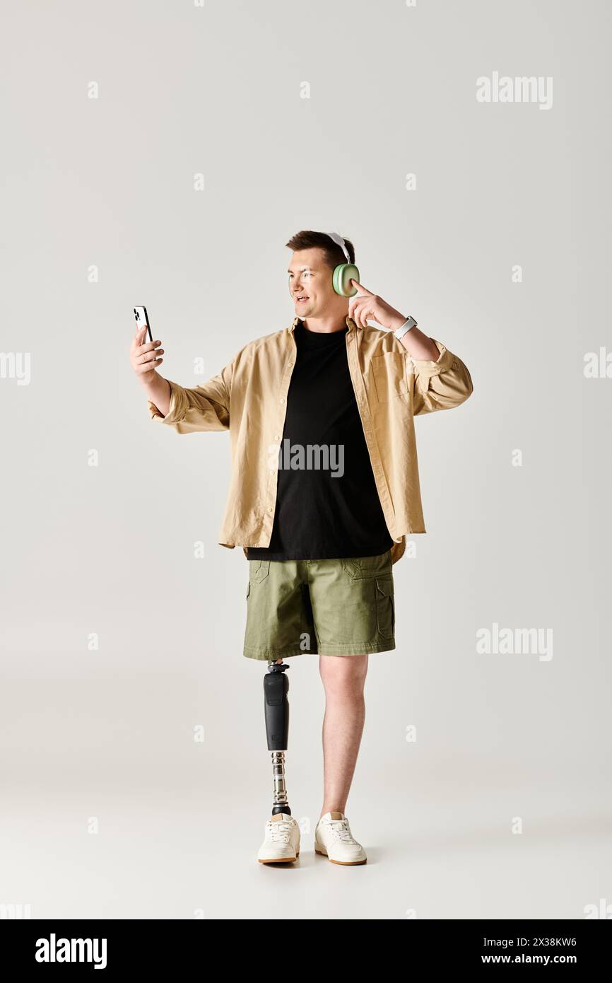 Un bel homme avec une jambe prothétique, portant une chemise noire et un short kaki, tient un téléphone portable. Banque D'Images