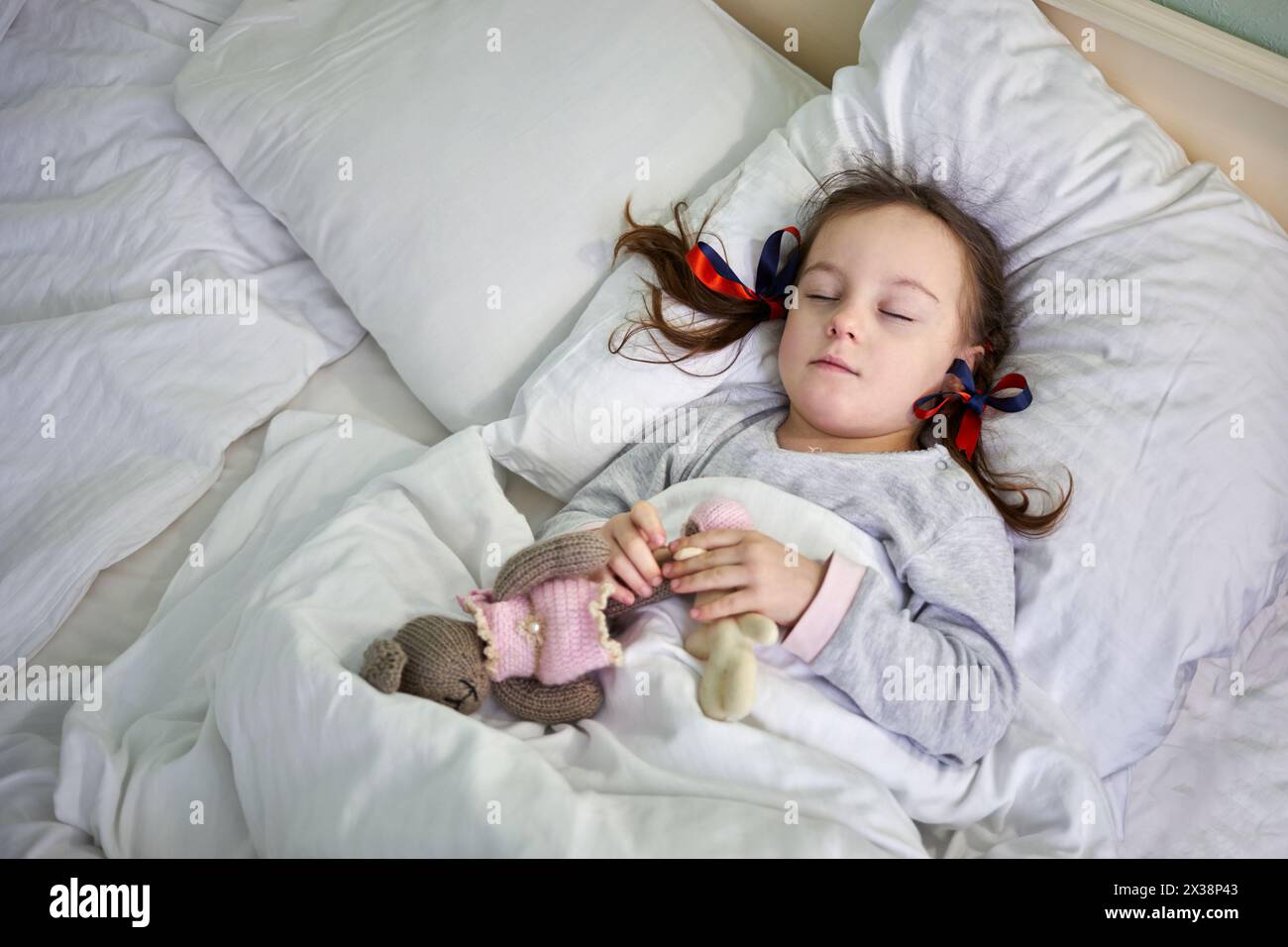 Petite fille dormant dans le lit et tenant le jouet mou dans les mains. Banque D'Images