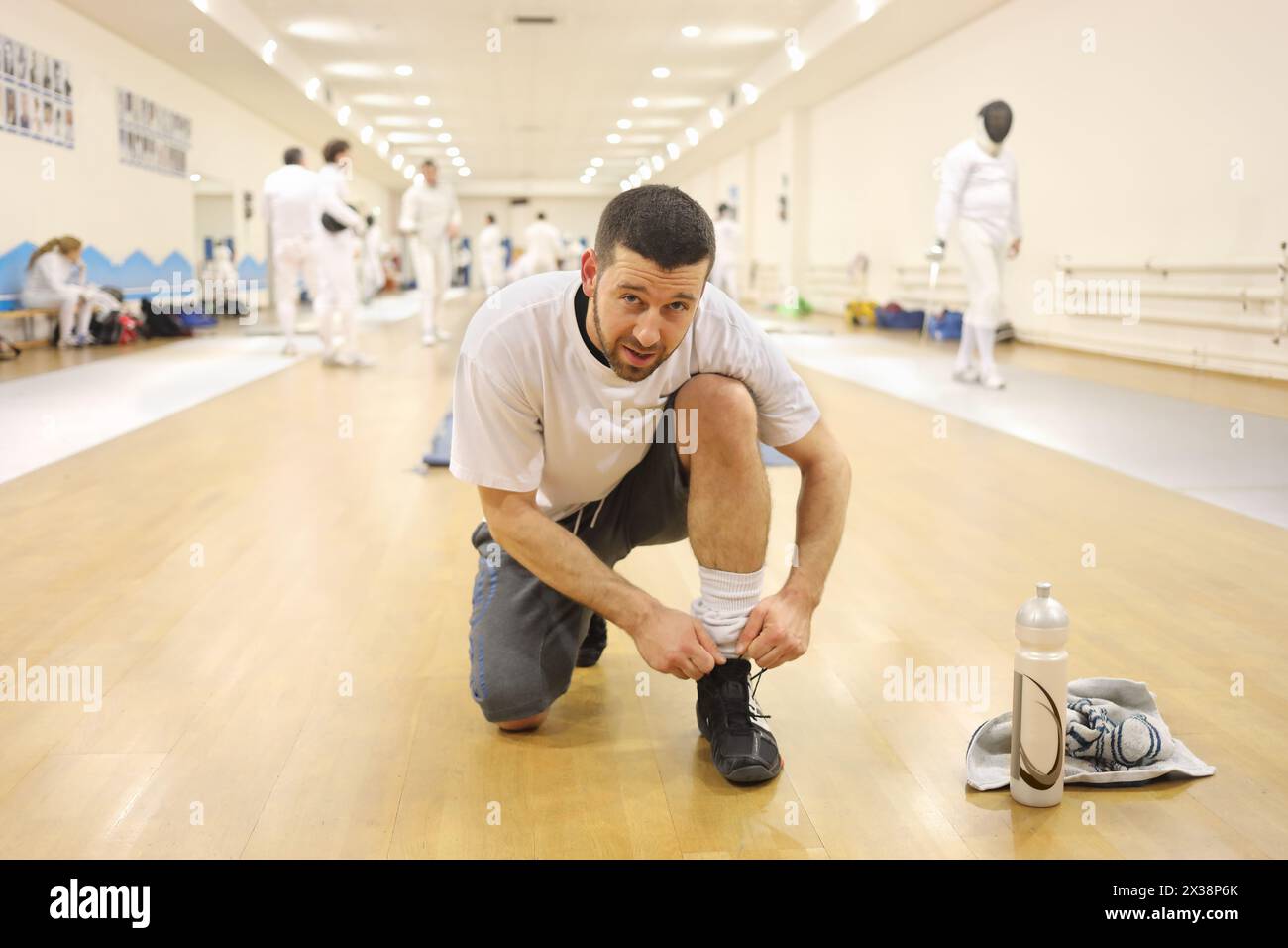 L'homme attache des lacets dans le gymnase pour l'entraînement d'escrime, d'autres personnes hors de la concentration Banque D'Images