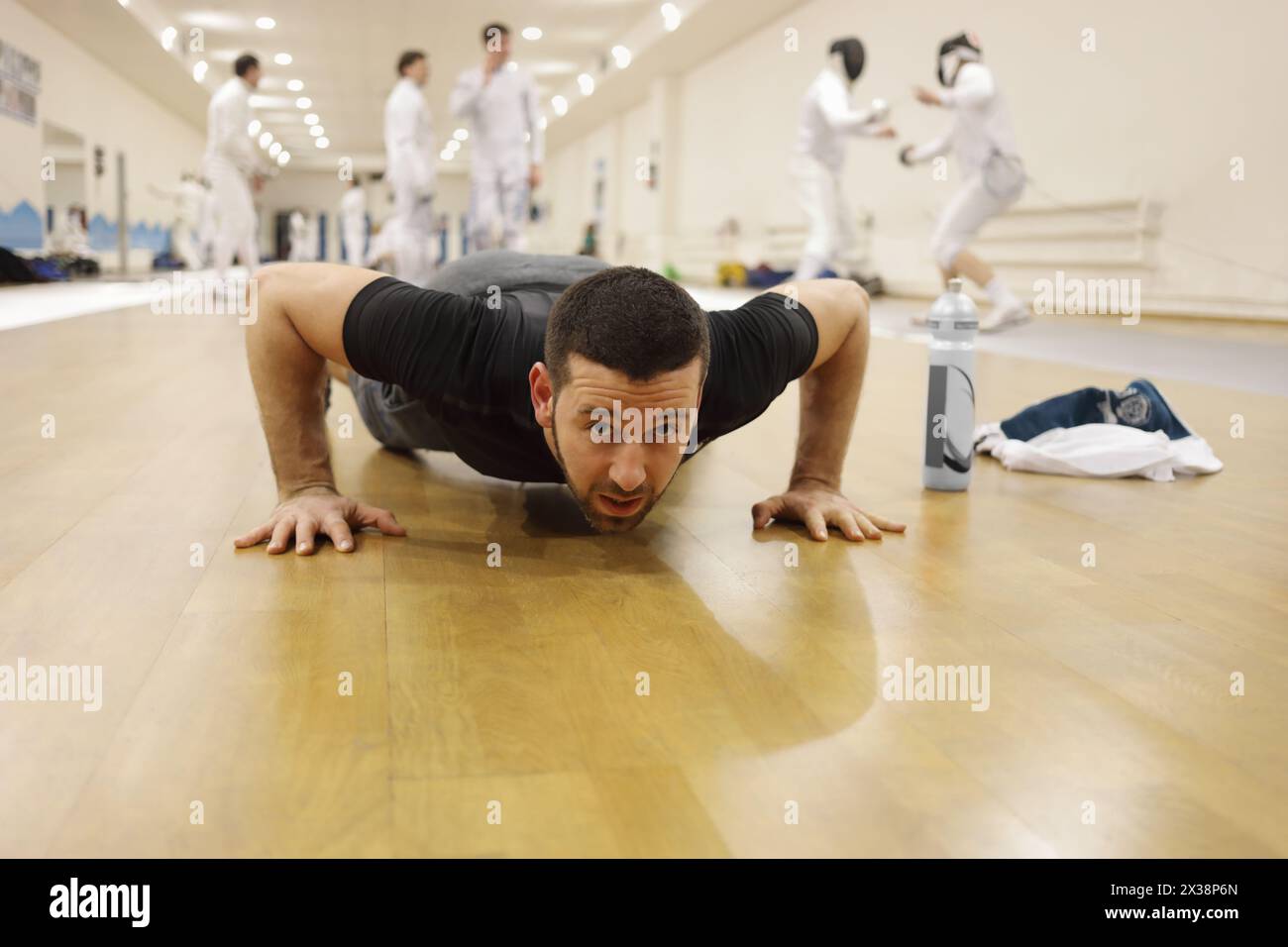 Homme press-up dans le gymnase pour la formation d'escrime, d'autres personnes hors de focus Banque D'Images