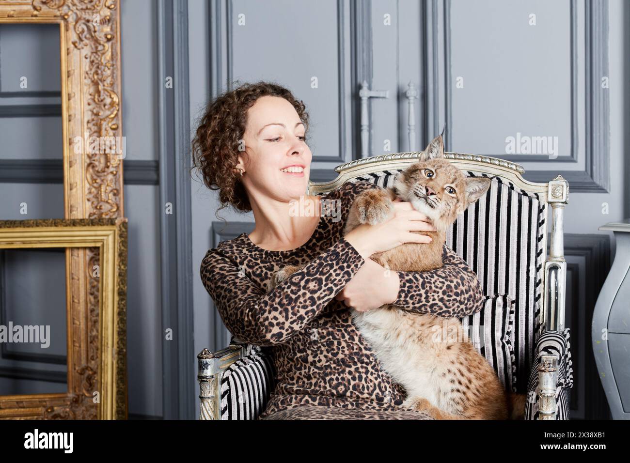 Femme en robe léopard joue avec lynx cub assis dans le fauteuil. Banque D'Images