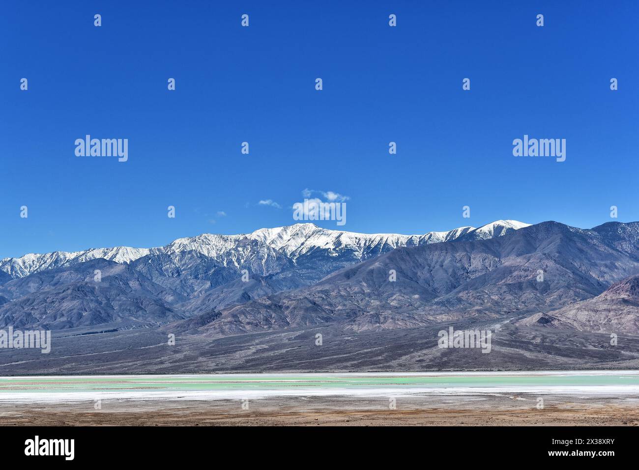 Les eaux vertes du lac au parcours de golf Devils avec les montagnes noires enneigées en arrière-plan, le parc national de la vallée de la mort. Banque D'Images