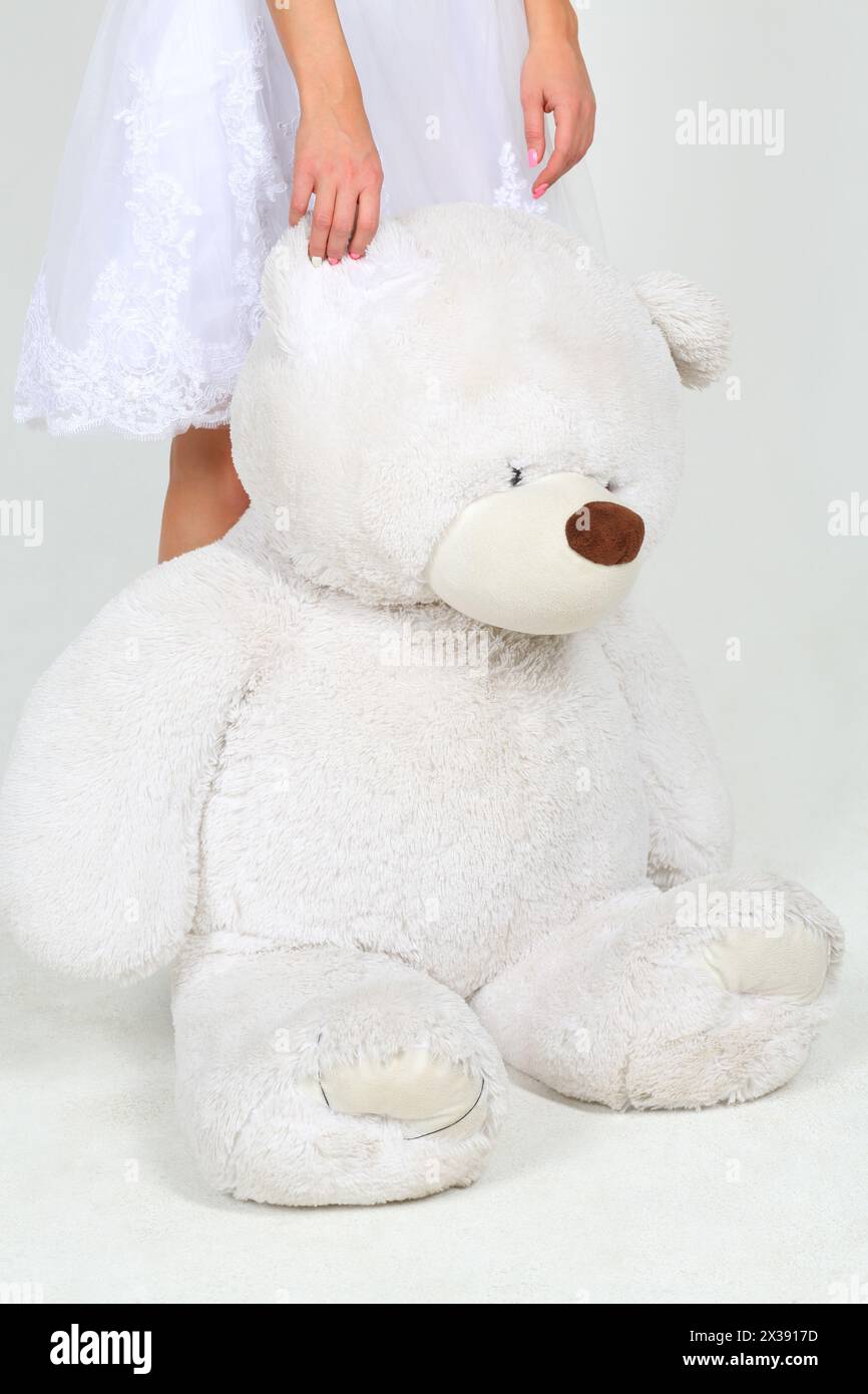 Femme en robe blanche se tient avec grand ours jouet dans le studio blanc, noface Banque D'Images