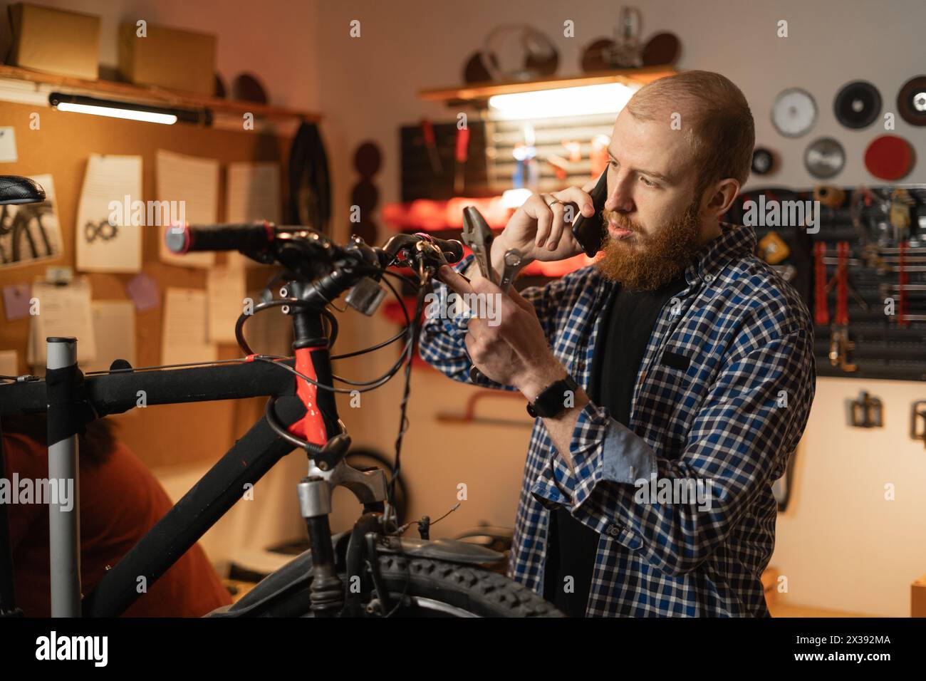 Homme mécanicien travaillant dans un atelier de réparation de vélos ou un garage, appel sur téléphone portable, technicien réparant vélo à l'aide d'un outil spécial Banque D'Images