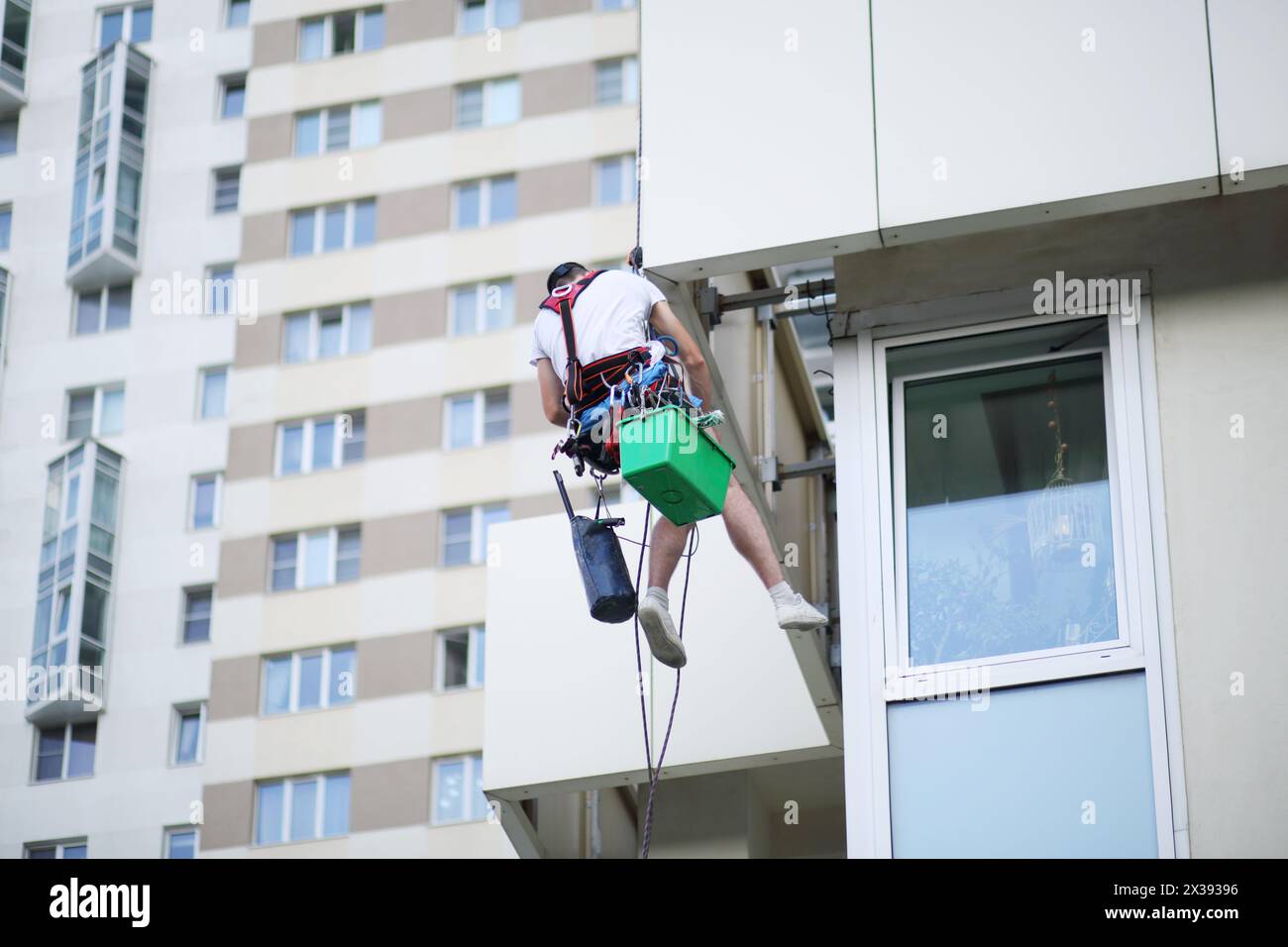 Homme accroche sur le câble de sécurité et nettoie la fenêtre du bâtiment résidentiel, vue arrière Banque D'Images