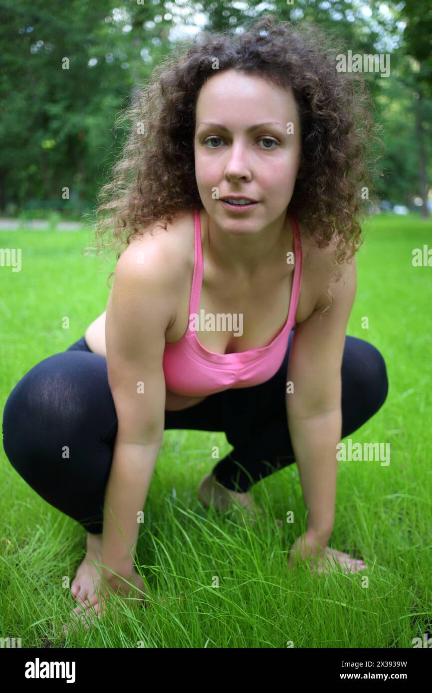 Femme en vêtements de sport pose sur la pelouse verte comme grenouille au jour d'été Banque D'Images