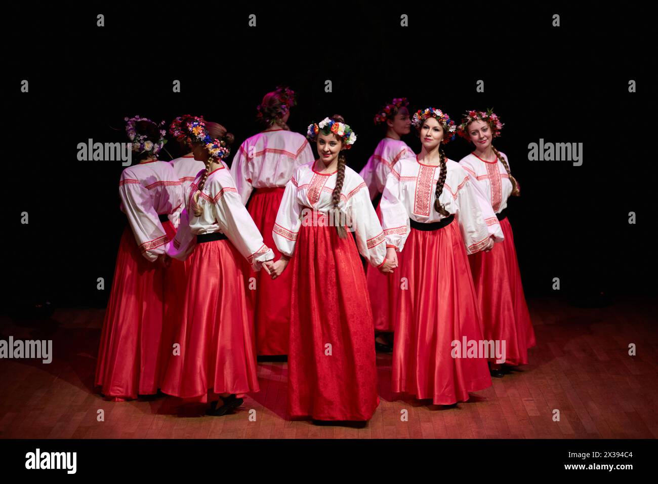 Huit filles en jupes rouges, chemisiers blancs brodés et avec des couronnes sur leurs têtes dansent la danse folklorique russe Banque D'Images