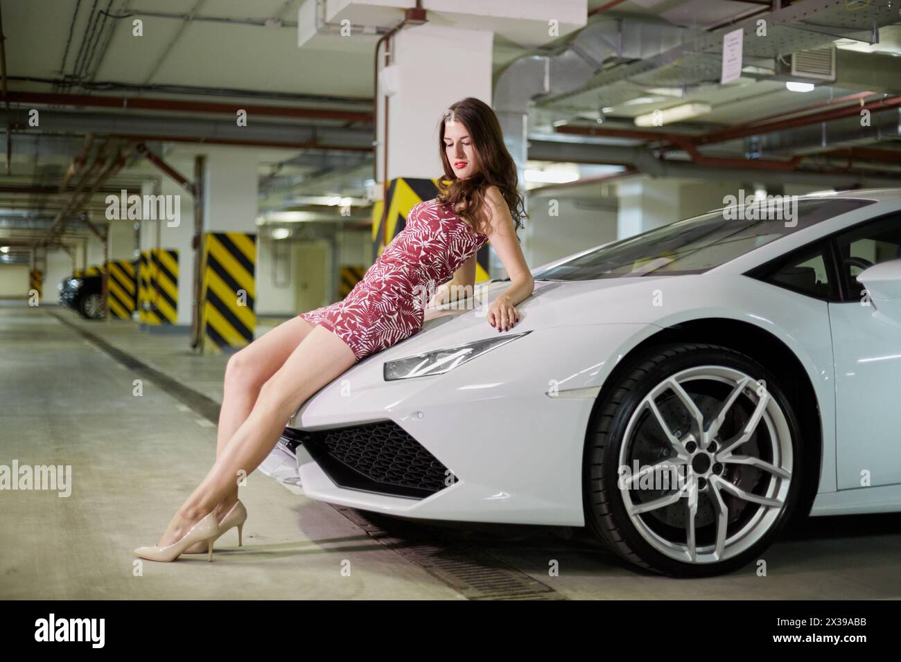 Jeune femme est assise sur le capot de la voiture blanche moderne au parking souterrain. Banque D'Images
