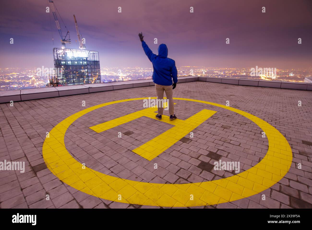 L'homme se tient sur l'héliport sur le toit d'un grand bâtiment dans la nuit avec en ville Banque D'Images