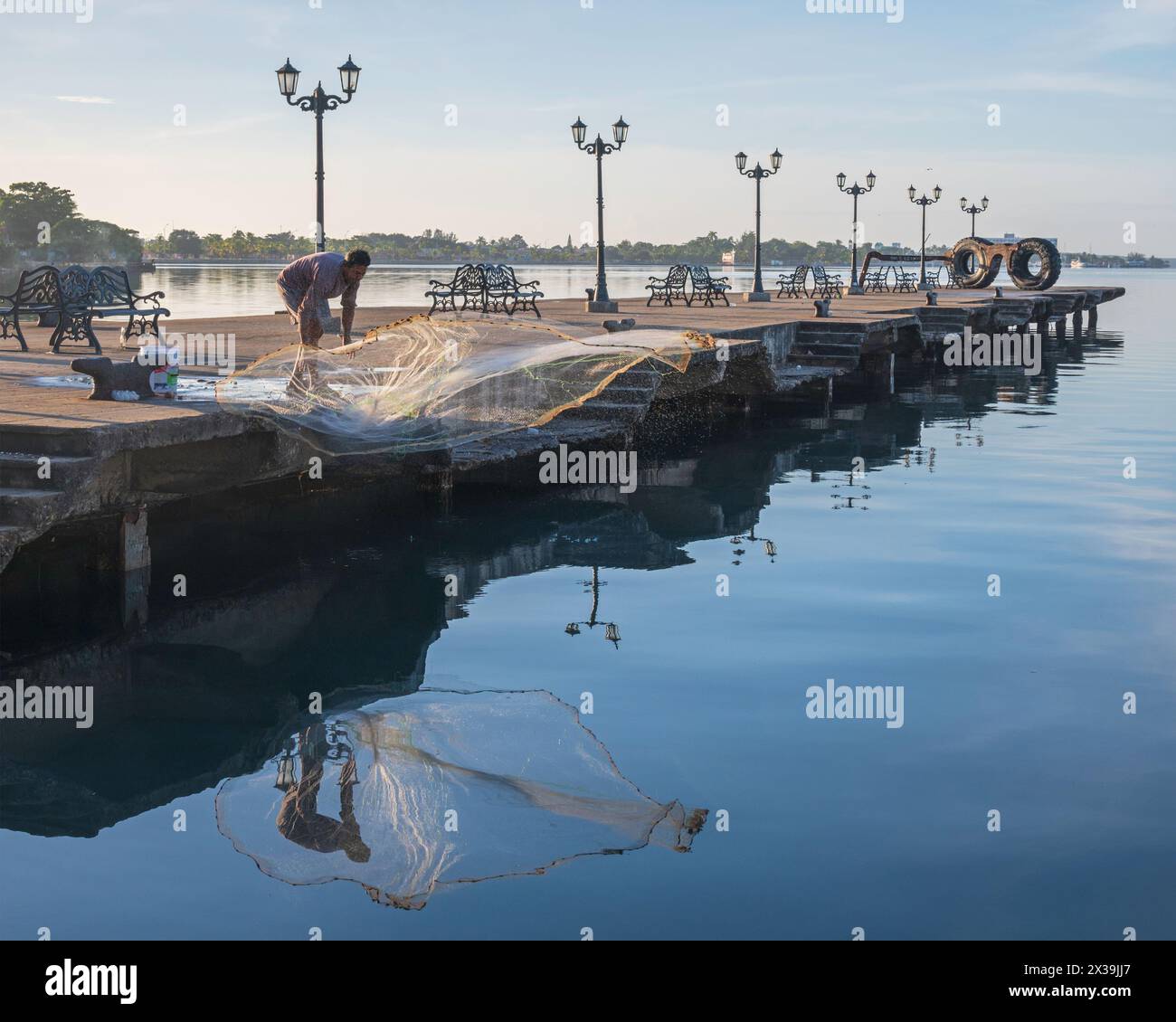 Homme jetant son filet de pêche de la jetée royale dans le port de Cienfuegos, Cuba, tôt le matin, juste après le lever du soleil. Banque D'Images