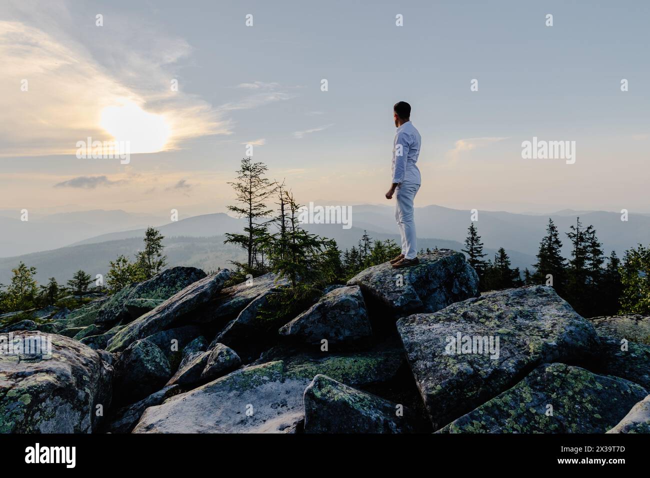 Un homme se tient confiant sur le sommet d'une montagne rocheuse, surplombant un vaste paysage en contrebas. Il semble petit contre le terrain accidenté, showcasin Banque D'Images