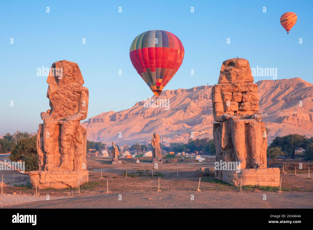 Montgolfières colorées survolant les colosses de Memnon au lever du soleil sur la Cisjordanie de Louxor, en Égypte Banque D'Images