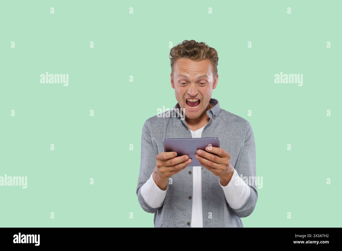 Un homme tient une tablette et la regarde avec une expression surprise. Il joue à un jeu ou regarde quelque chose sur l'écran Banque D'Images