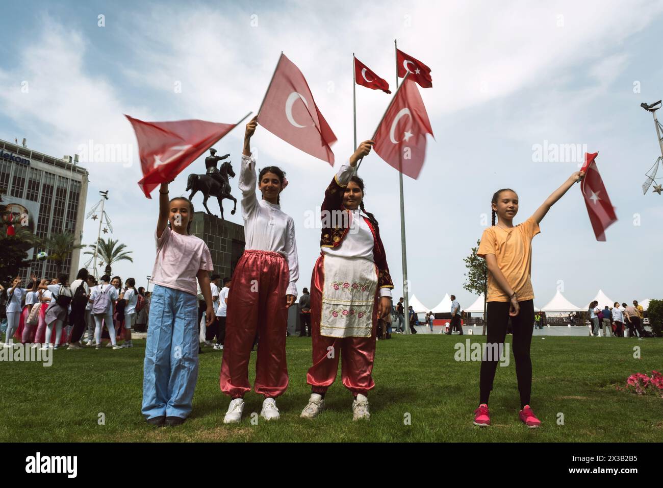 Izmir, Turquie - 23 avril 2024 : quatre filles joyeuses agitent le drapeau turc pendant les festivités de la Journée de l’enfance avec des robes de démonstration traditionnelles, Banque D'Images