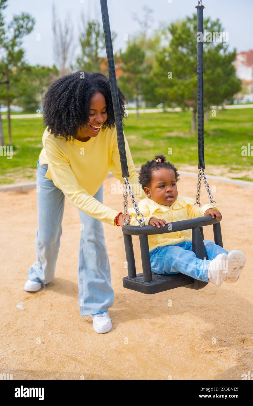 Photo verticale d'une fille africaine heureuse et mère dans le parc balançant et souriant Banque D'Images