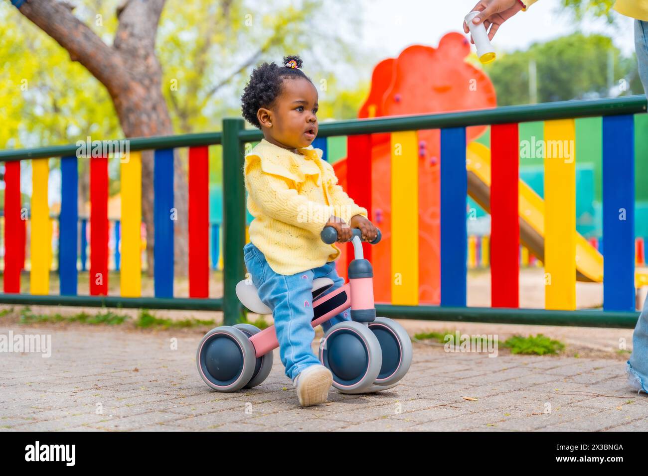 Photo pleine longueur d'une jolie petite fille africaine chevauchant un vélo jouet dans un parc Banque D'Images