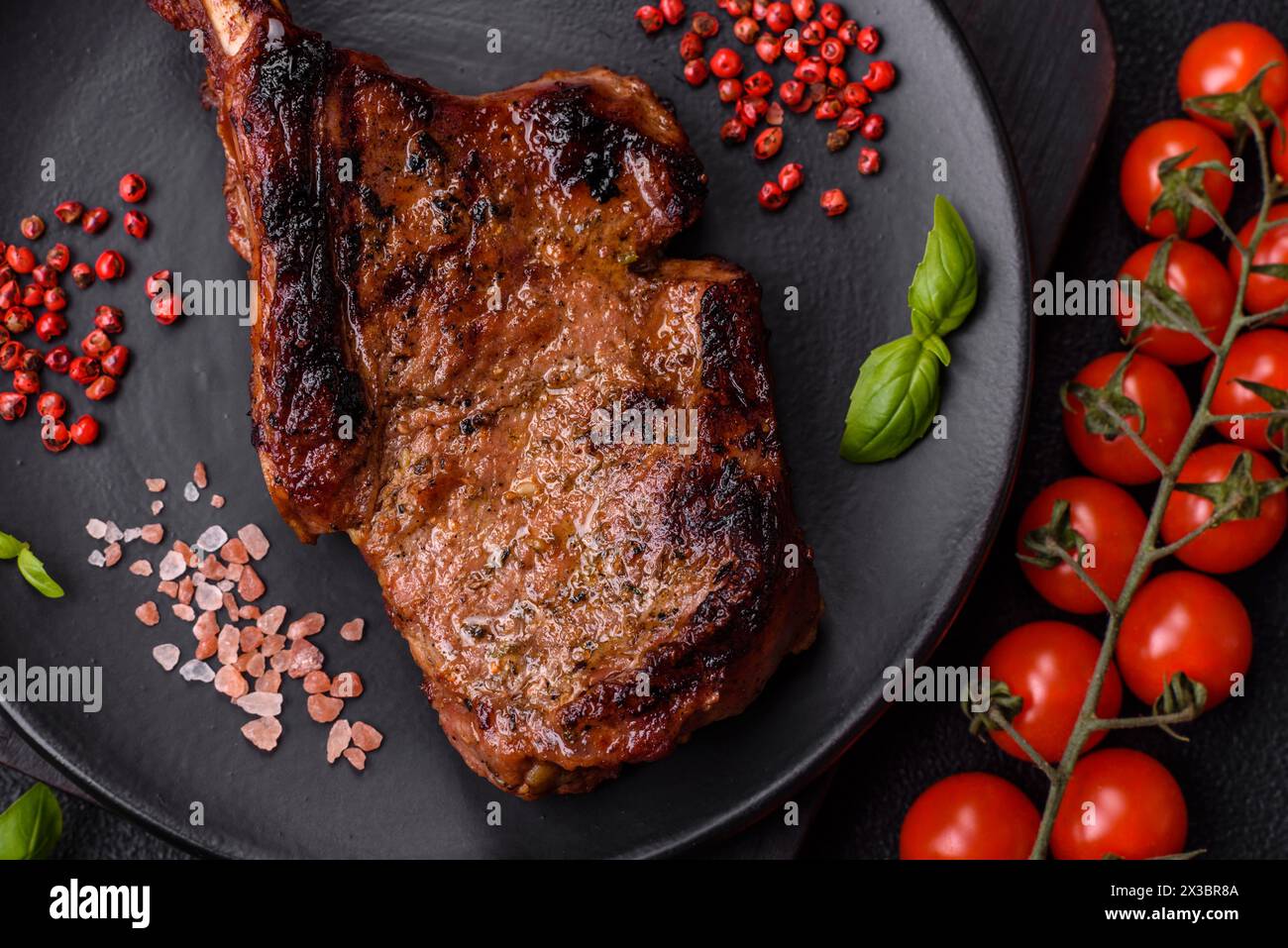 Délicieux steak de bœuf juteux sur l'os, tomahawk avec du sel, des épices et des herbes sur un fond de béton foncé Banque D'Images