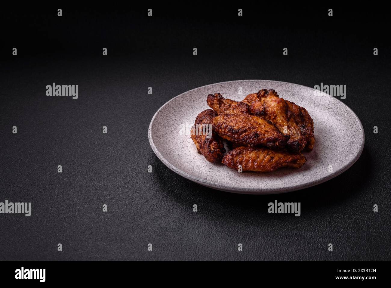 Délicieuses ailes de poulet juteuses cuites sur le gril avec du sel, des épices et des herbes sur un fond de béton foncé Banque D'Images