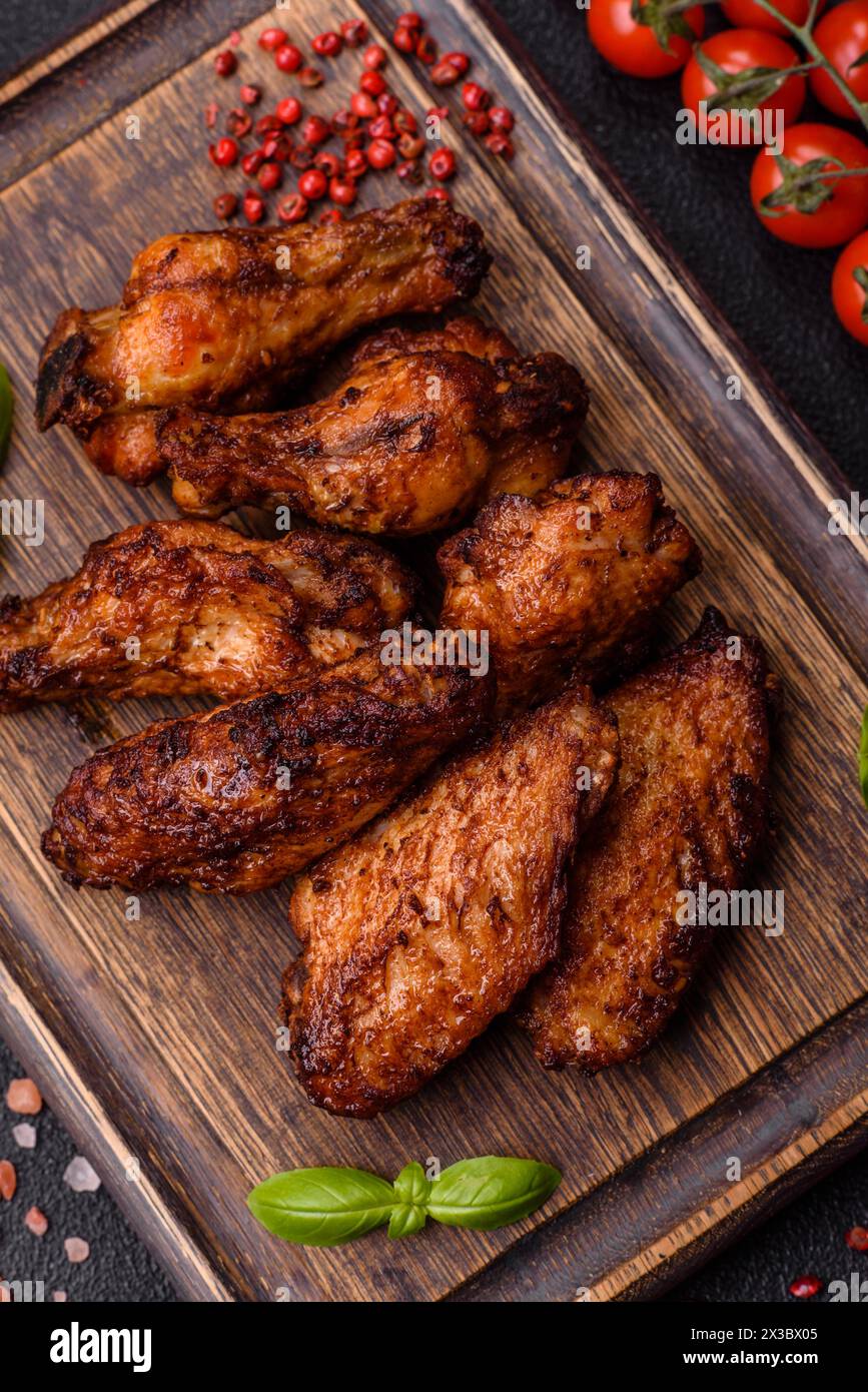 Délicieuses ailes de poulet juteuses cuites sur le gril avec du sel, des épices et des herbes sur un fond de béton foncé Banque D'Images