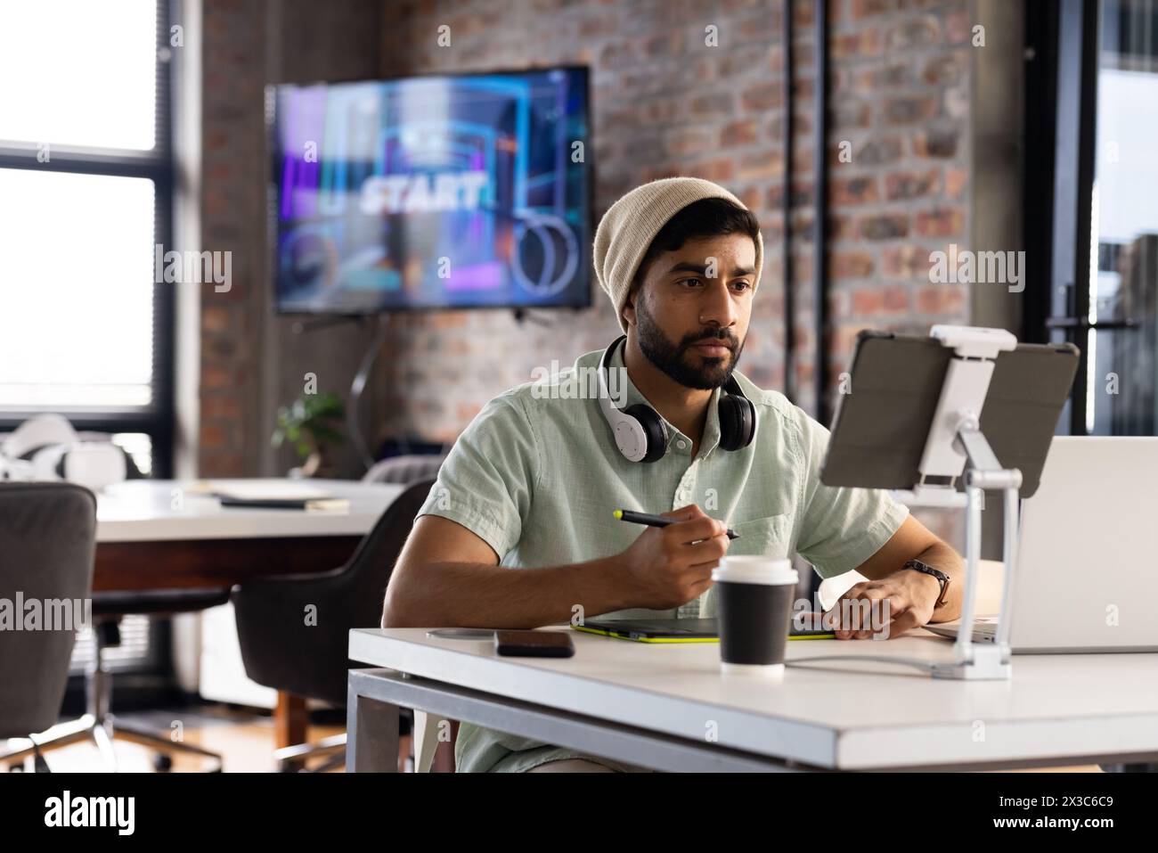 Jeune homme professionnel asiatique portant des écouteurs, tenant un stylo, regardant une tablette dans un busi moderne Banque D'Images