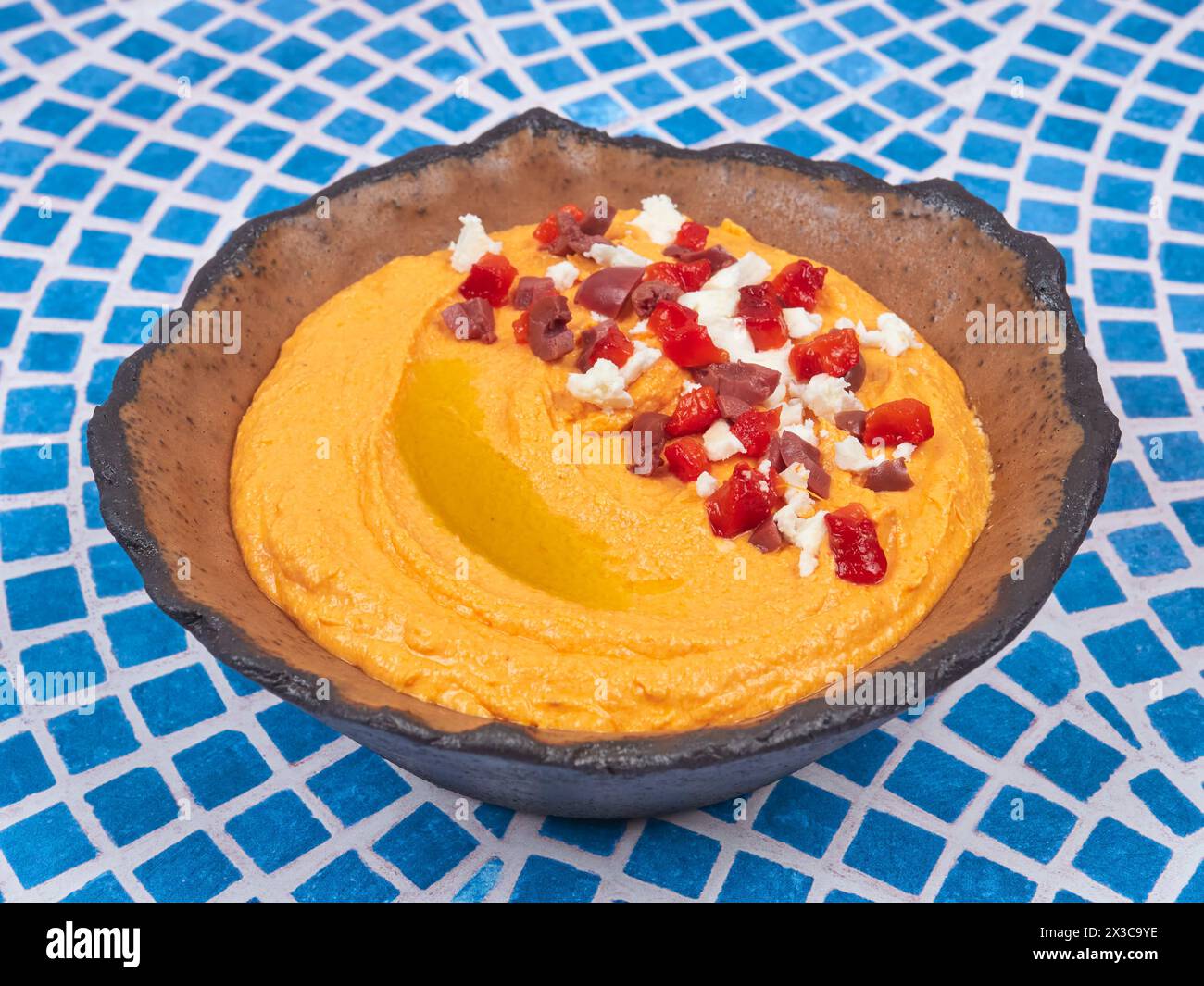 Htipiti, un apéritif grec à base de fromage feta et de poivrons rouges rôtis, dans un bol en céramique, sur une table en mosaïque bleue et blanche Banque D'Images