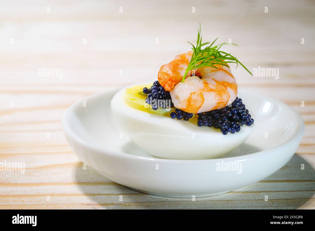 Oeufs durs coupés en deux avec caviar noir, crevettes et garniture d'aneth sur une petite assiette blanche et une table en bois, snack de doigt pour les vacances comme Pâques, CH Banque D'Images