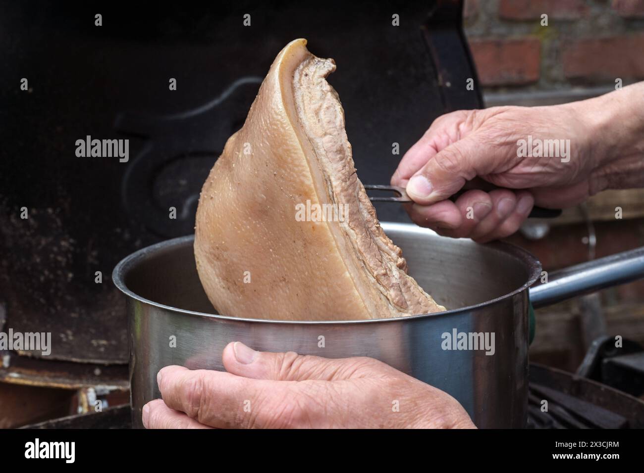 Cook prend un morceau de viande de croûte cuit lentement hors de la casserole pour faire une sauce bouillon dans une cuisine rustique, espace de copie, foyer sélectionné, profondeur étroite de fi Banque D'Images