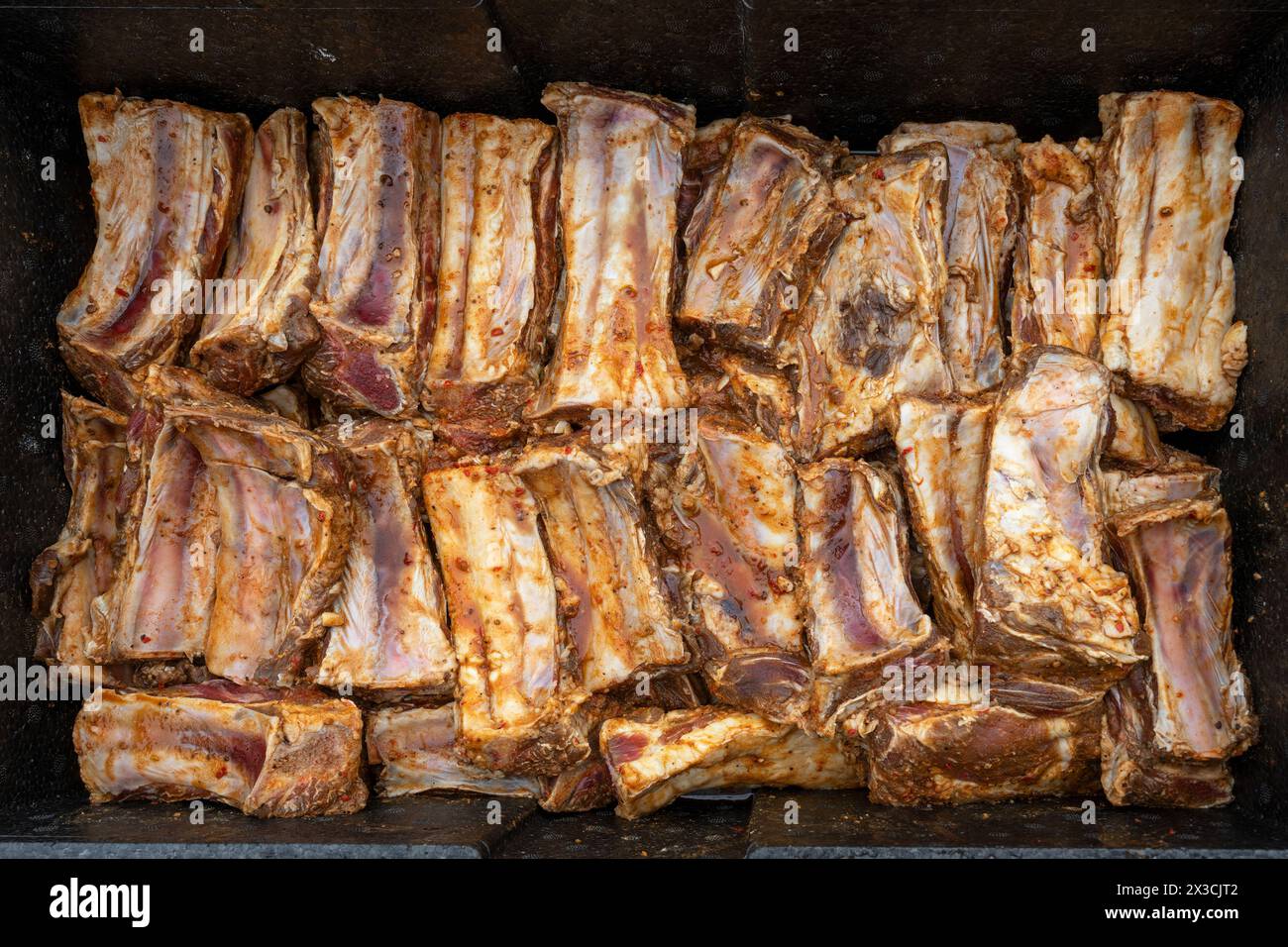 Les côtes courtes de bœuf assaisonnées et marinées sont placées dans un grand bol en métal noir, préparation pour une partie barbecue avec de nombreux invités, vue de dessus, Banque D'Images