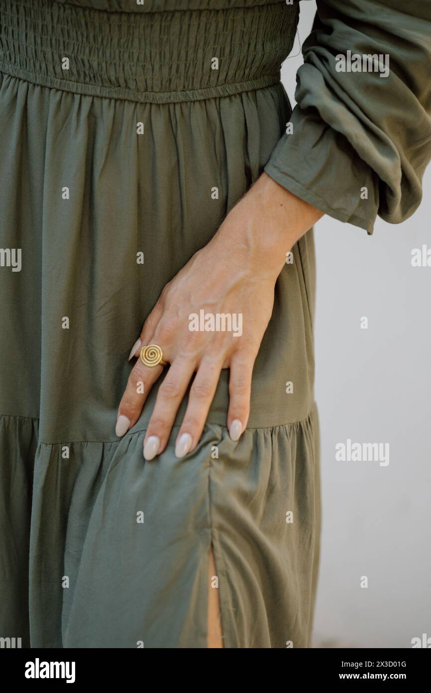 Détail robe olive, main avec un anneau en spirale, élégance subtile. Banque D'Images