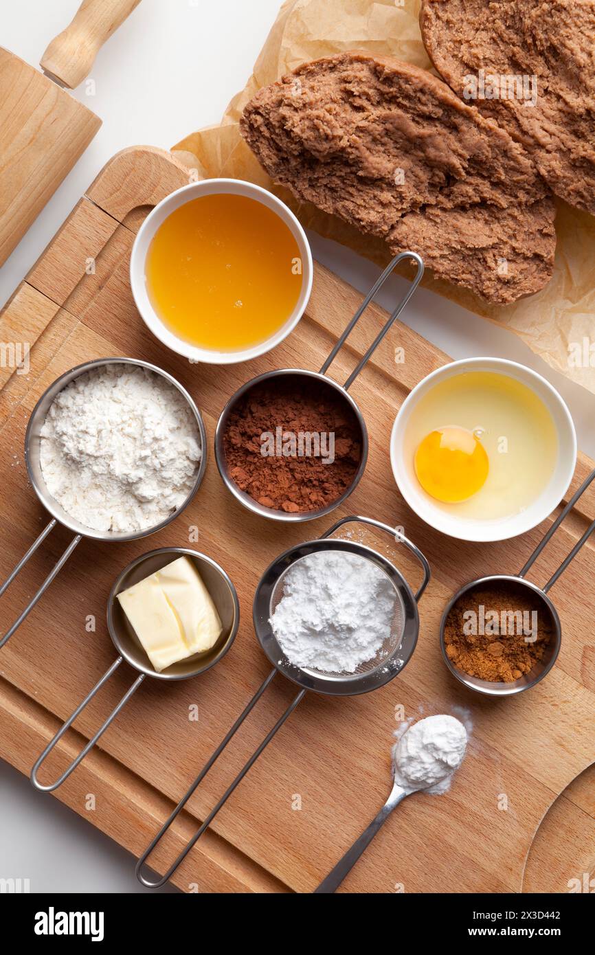 Pâte à pain d'épices pour Noël et ingrédients pour faire la pâte - oeuf, miel, épice, sucre en poudre, beurre, cacao, farine, bicarbonate de soude sur un ba en bois Banque D'Images