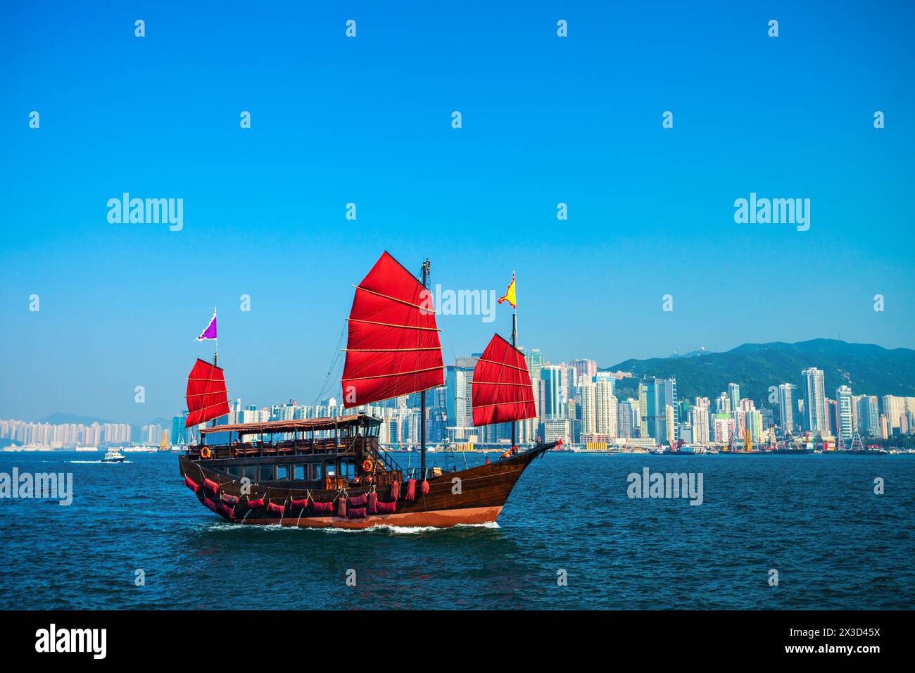 Bateau de croisière touristique de style traditionnel avec voiles rouges traverse le port Victoria de Kowloon à l'île de Hong Kong Banque D'Images