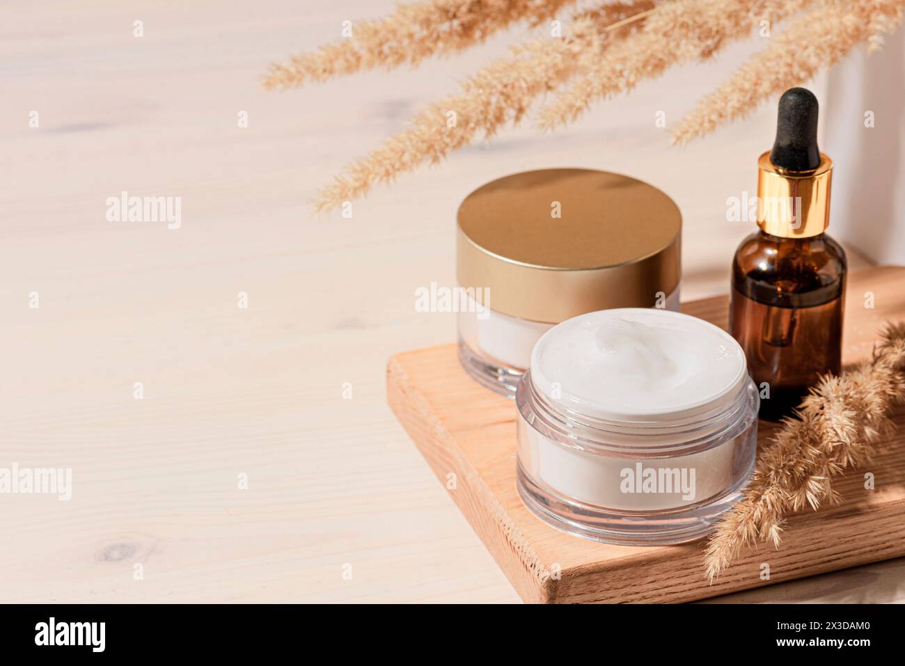Sérum cosmétique et produits de crème de beauté avec des roseaux secs ou de l'herbe de pampa sur fond beige en bois, plan tendance avec des ombres dures. Soin du visage n Banque D'Images