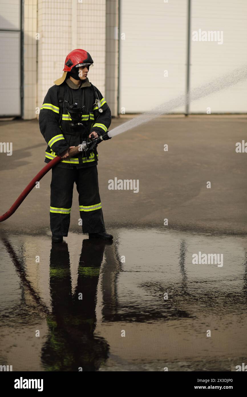 portrait pleine hauteur des prises de pompier et ajuster la buse et le tuyau d'incendie pulvérisant de l'eau à haute pression Banque D'Images