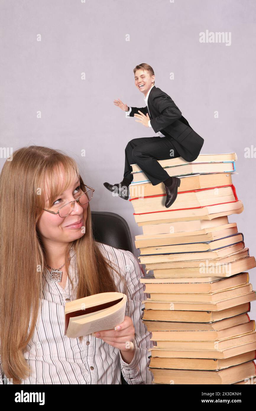 Collage avec la jeune jolie fille lit le livre à haute voix au petit homme d'affaires assis sur pile de livres, tout le monde est souriant Banque D'Images