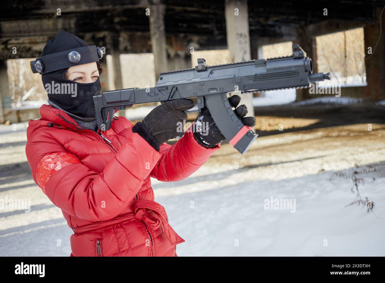 Femme en veste rouge et masque de ski visant avec pistolet de jeu en plein air le jour d'hiver. Banque D'Images
