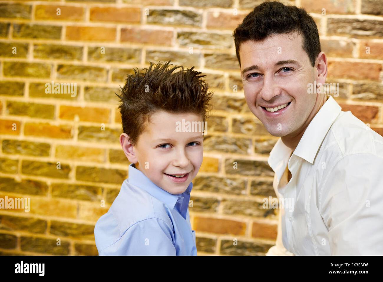 Portrait d'homme et garçon souriant contre un mur de briques rouges. Banque D'Images