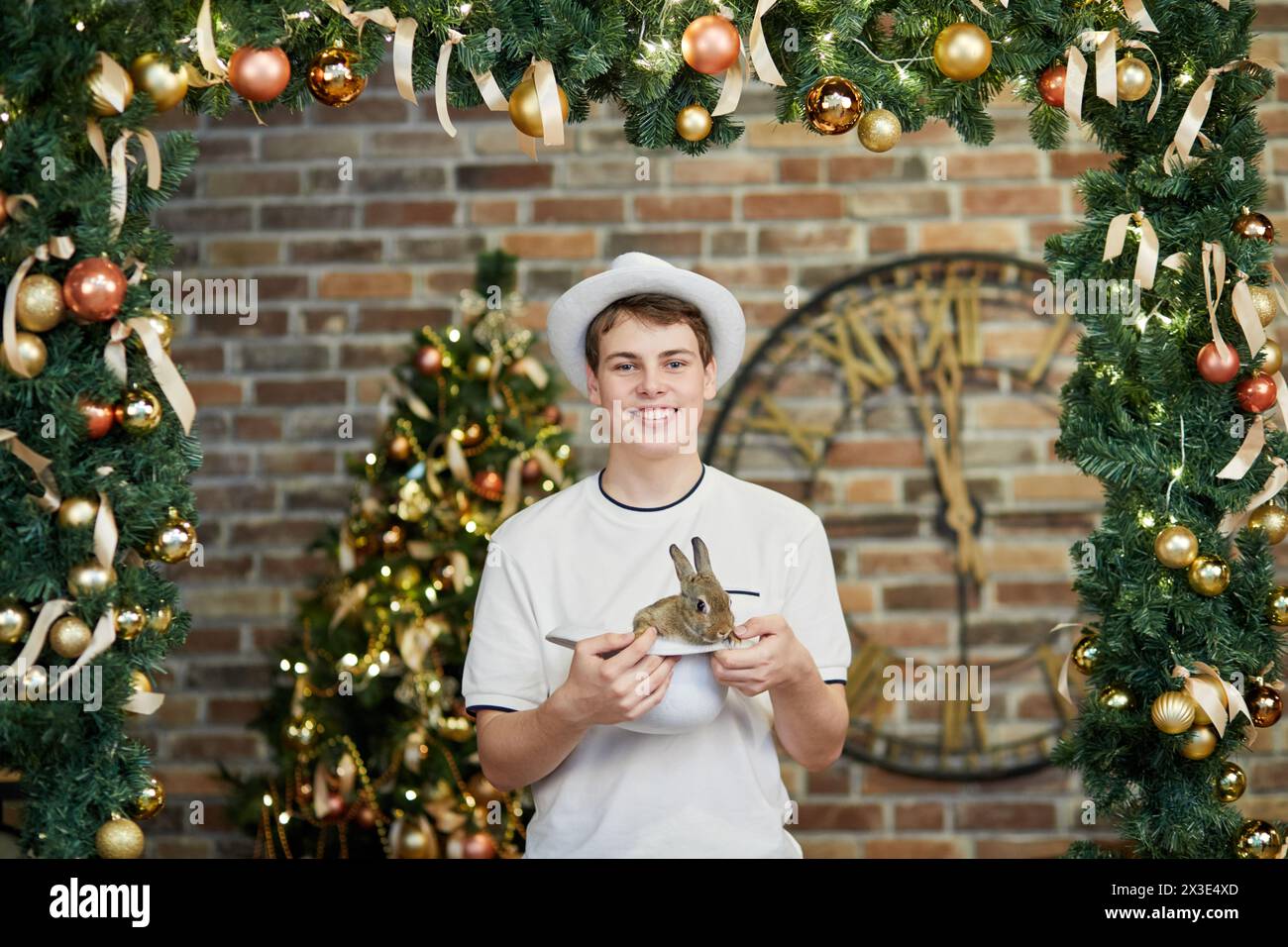 Garçon souriant dans les stands de chapeau blanc tenant un autre chapeau avec lapin dans la chambre décorée pour les vacances de Noël. Banque D'Images
