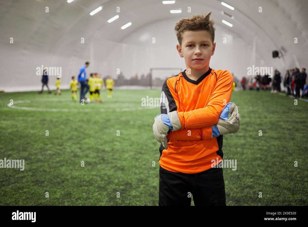 Garçon en uniforme de sport avec des gants de gardien de but sur les mains debout sur le terrain de football intérieur. Banque D'Images