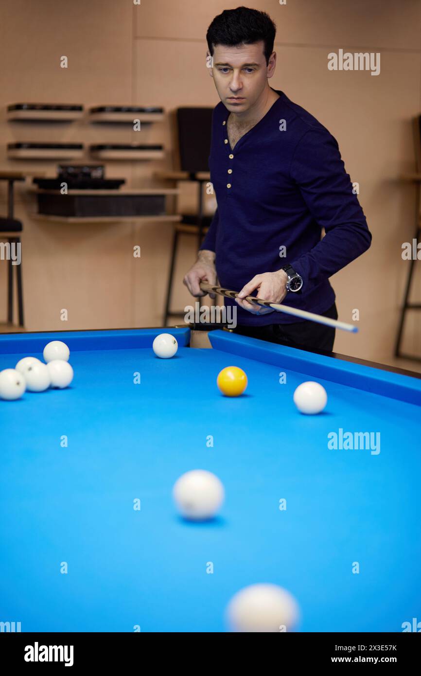 Homme en chemise bleu foncé regarde la table de billard avec des balles dans le club. Banque D'Images