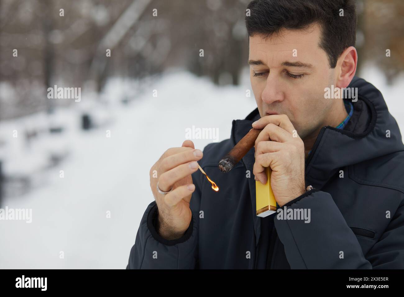 Homme lumières et bouffées au cigare dans le parc enneigé d'hiver. Banque D'Images