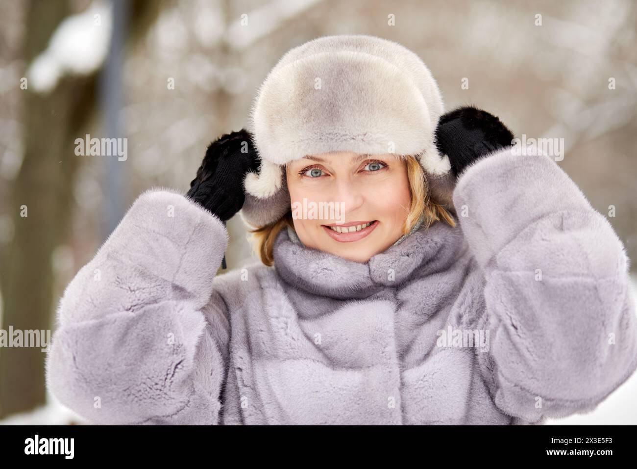 Gros plan portrait de femme souriante en chapeau et manteau de fourrure et moufles tricotées dans le parc d'hiver. Banque D'Images