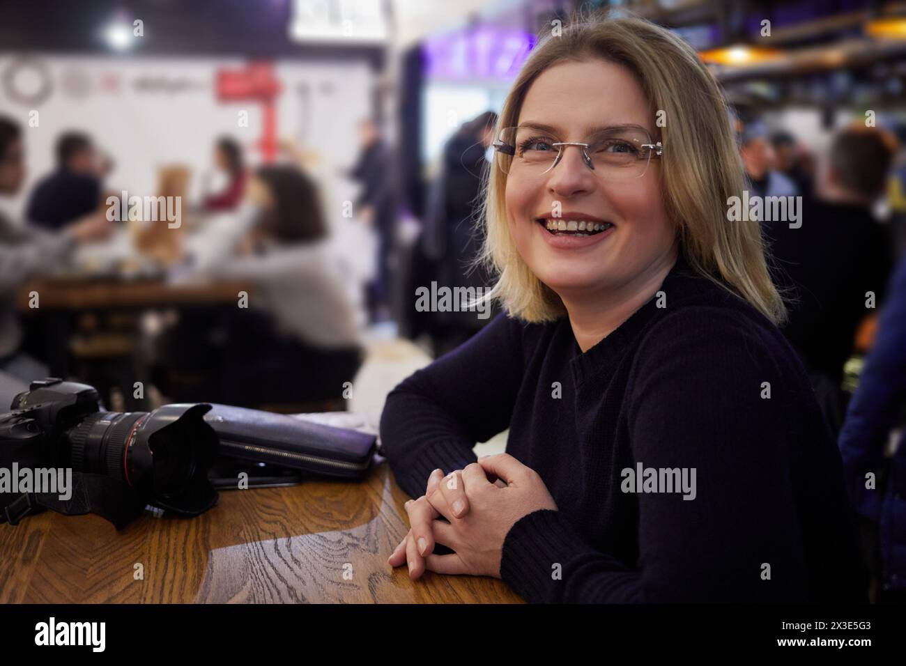 Femme souriante dans des lunettes est assis à table avec caméra dans le café. Banque D'Images