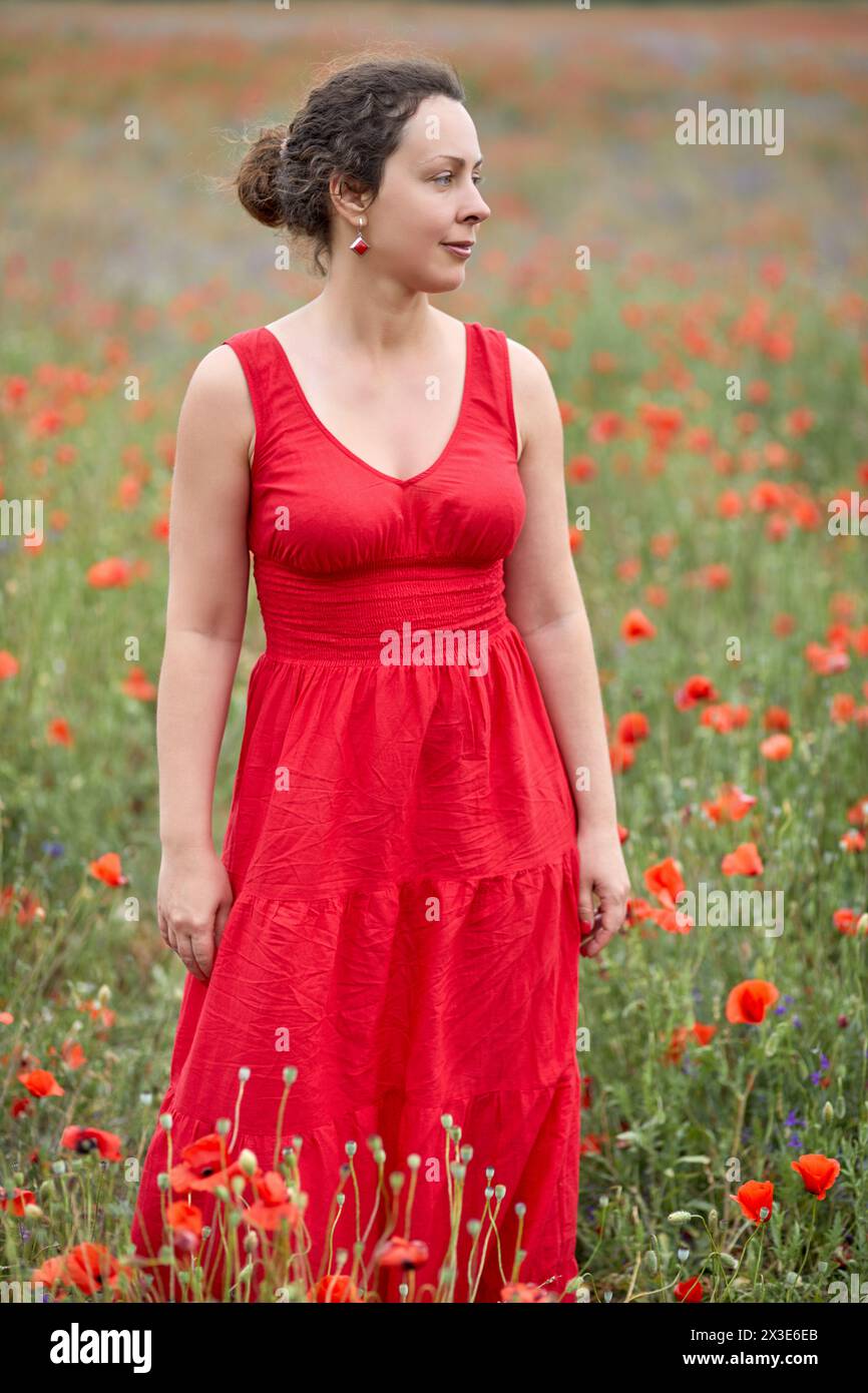 Femme en robe rouge se tient sur le champ de coquelicots rouges. Banque D'Images