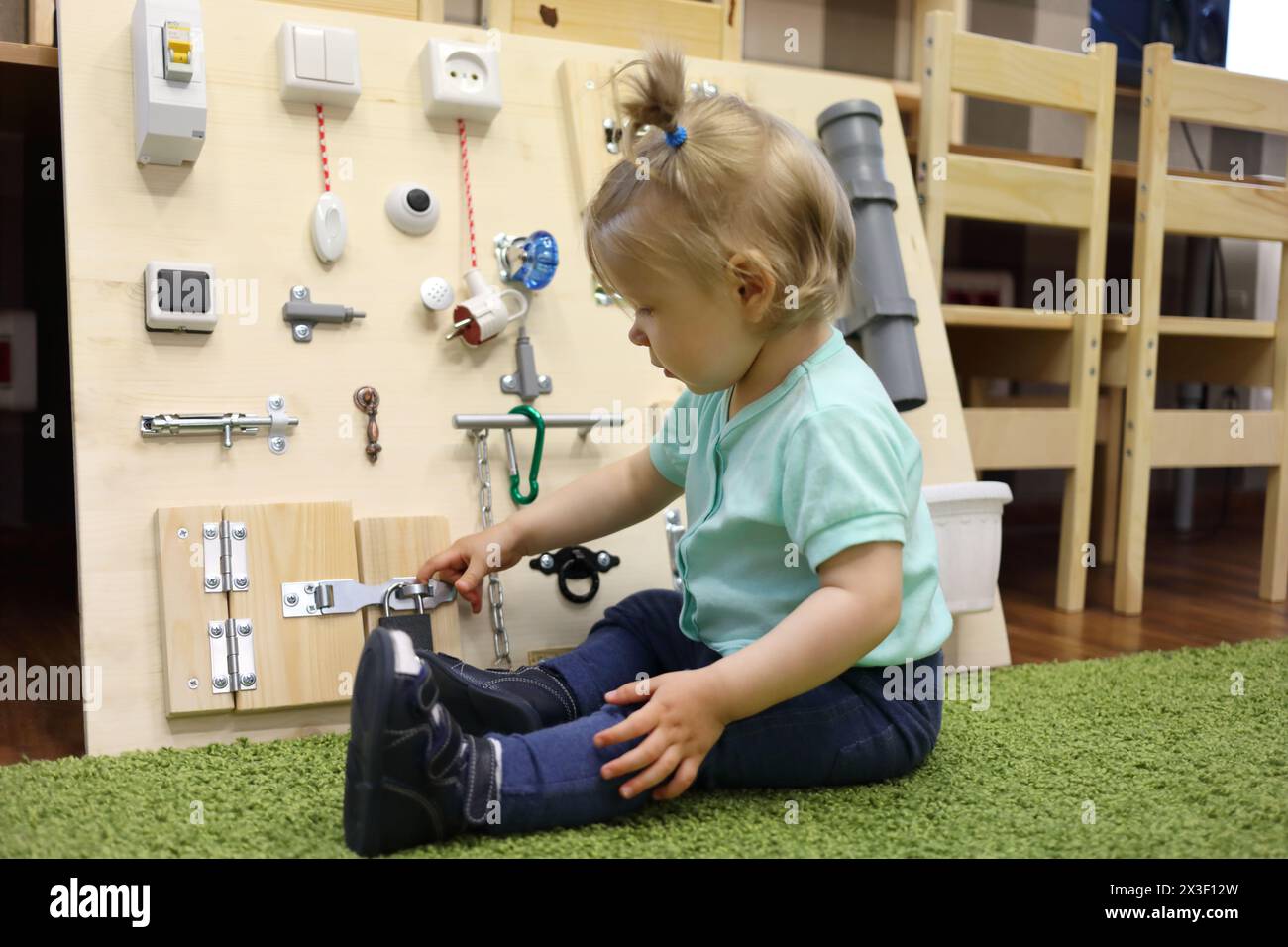 Petite fille joue sur le tapis avec un conseil occupé dans la maternelle moderne Banque D'Images