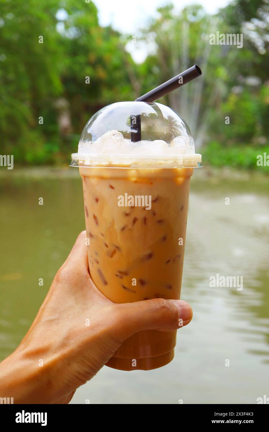 Main tenant une tasse de thé glacé thaïlandais savoureux avec fontaine en toile de fond Banque D'Images