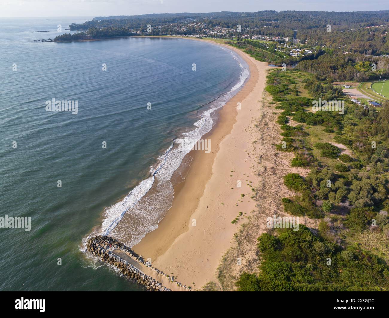 Vue aérienne d'un brise-lames à l'extrémité d'une longue plage de sable avec de douces vagues qui roulent dans Batemans Bay en Nouvelle-Galles du Sud, Australie. Banque D'Images